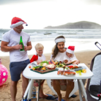 An Australian family having a Christmas bbq on the beach. Santa is surfing in the background